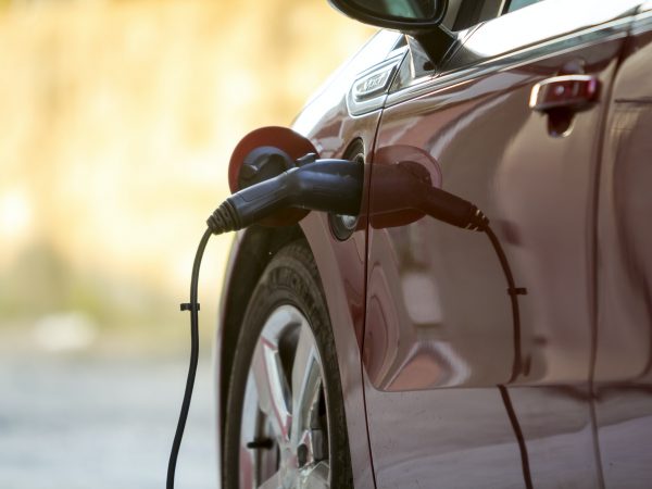 Carro elétrico sendo recarregado na rua ensolarada. Cabo carregador
